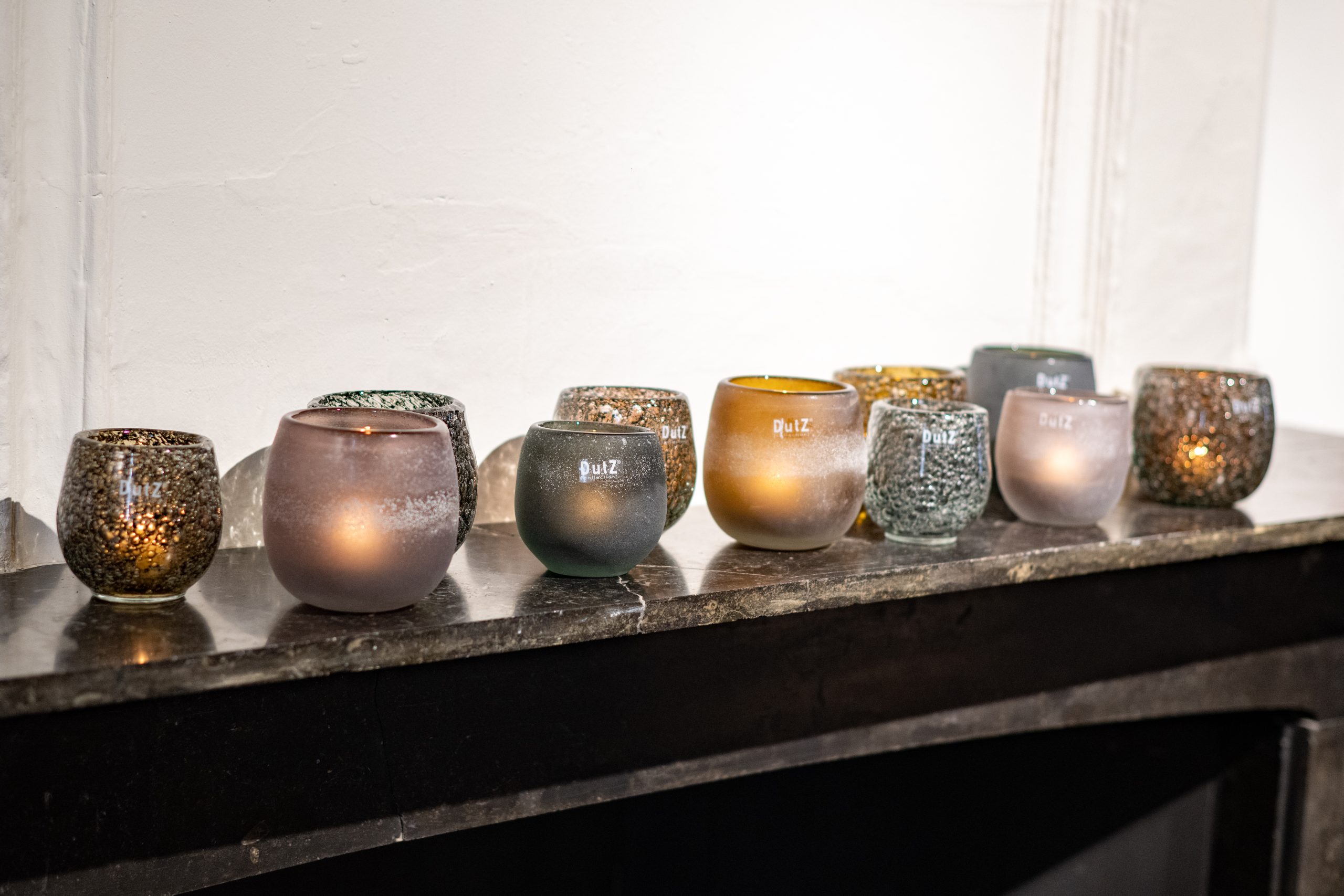 Hurricane Diva en Hurricane Diva Antic op een schoorsteenmantel. De kleuren zijn, amber, aubergine, olivegrey en grey. In de Hurricanes branden kaarsen